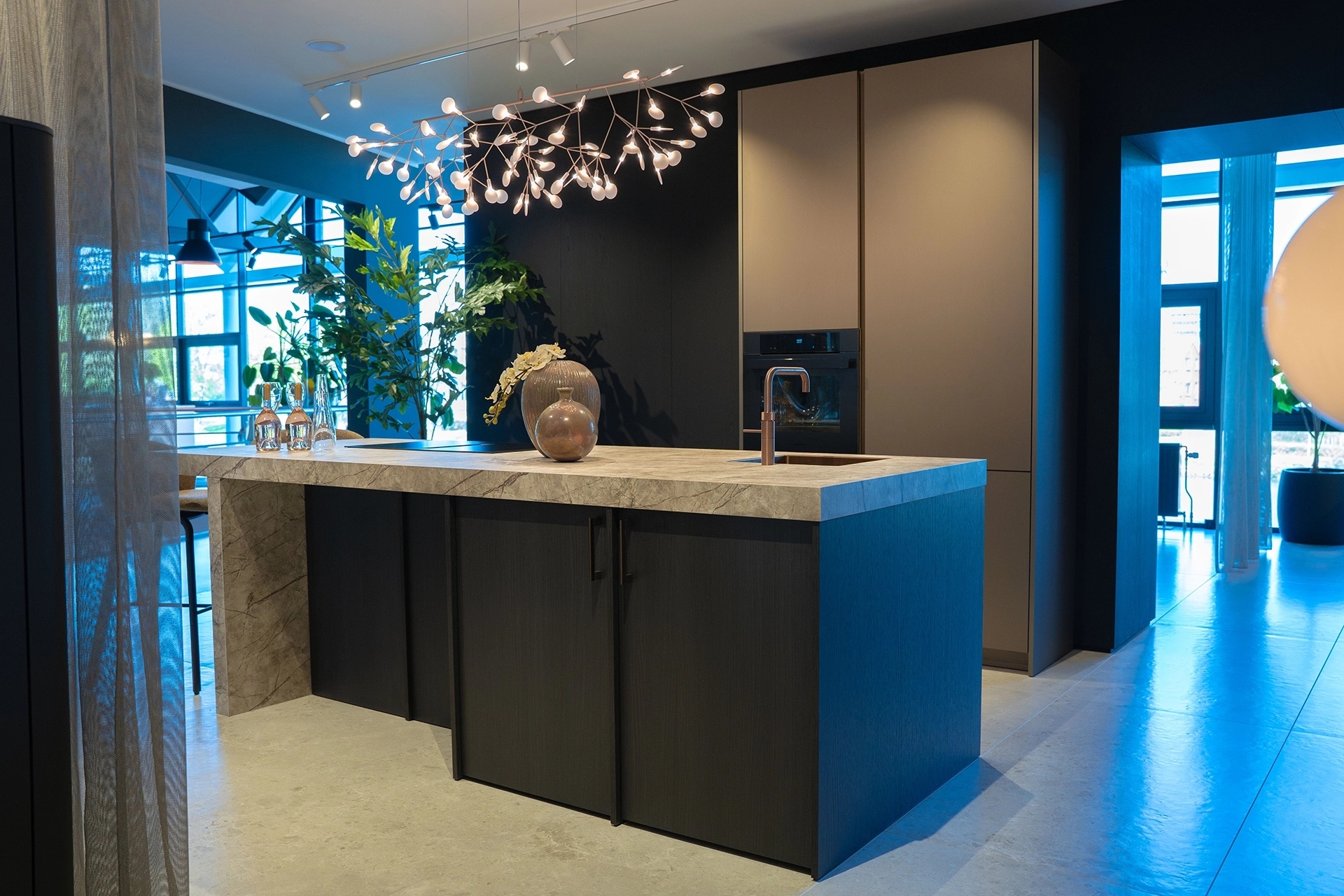 Moderne keuken in de showroom van Intermat Alphen aan den Rijn met donker kookeiland, natuursteenlook werkblad en hoge kasten